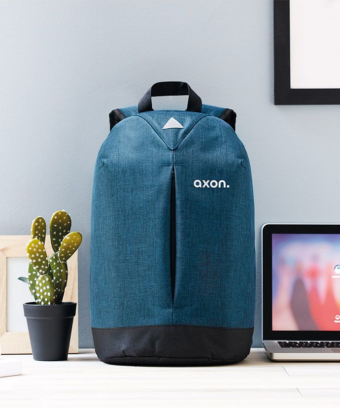 Blauer Rucksack mit Aufdruck auf einem Tisch mit Laptop und einer Pflanze. Werbeartikel für internes Marketing.